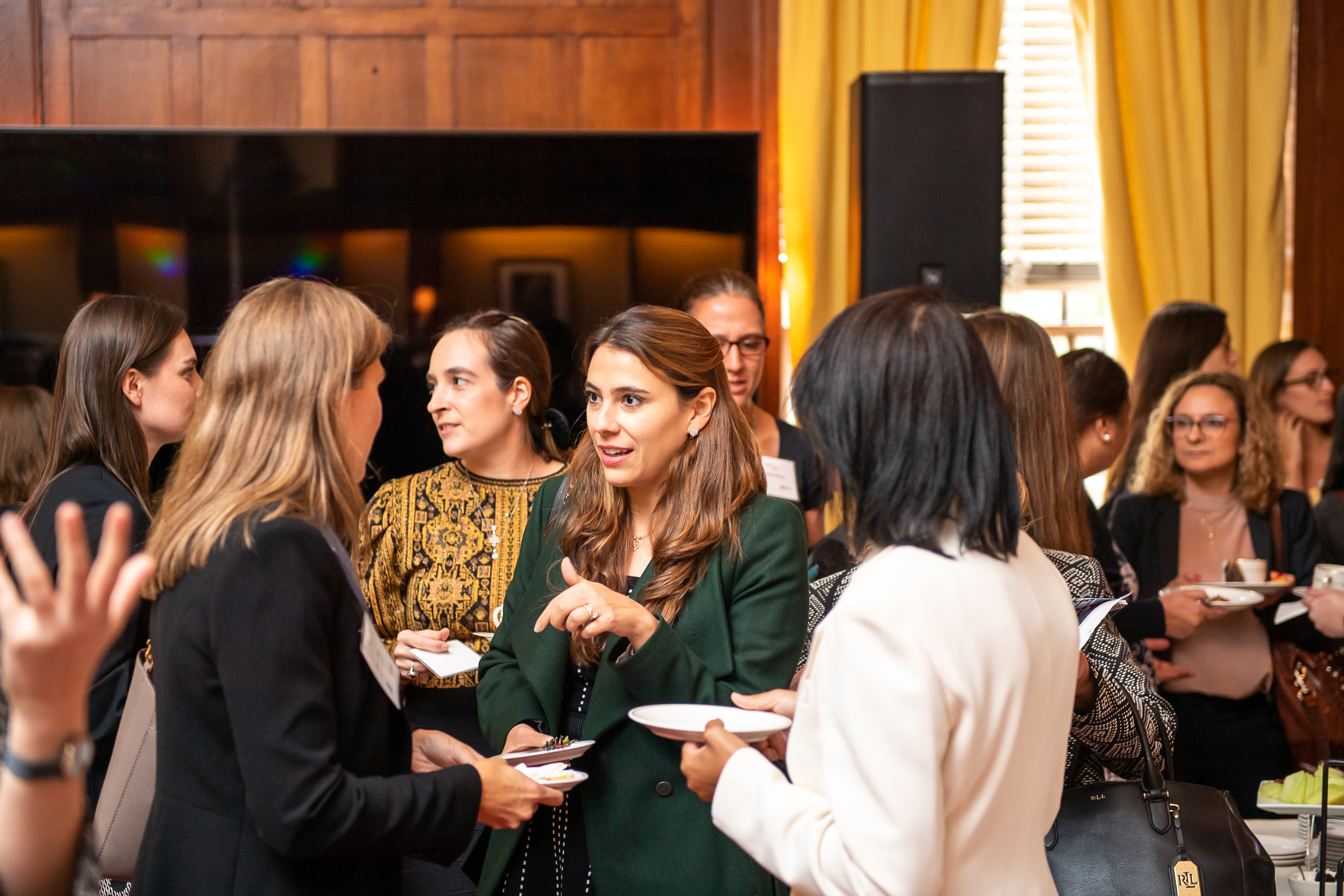 A group of three women talk in the middle of a busy meeting room