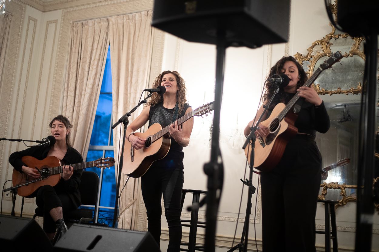 Three artists holding guitars and performing on stage