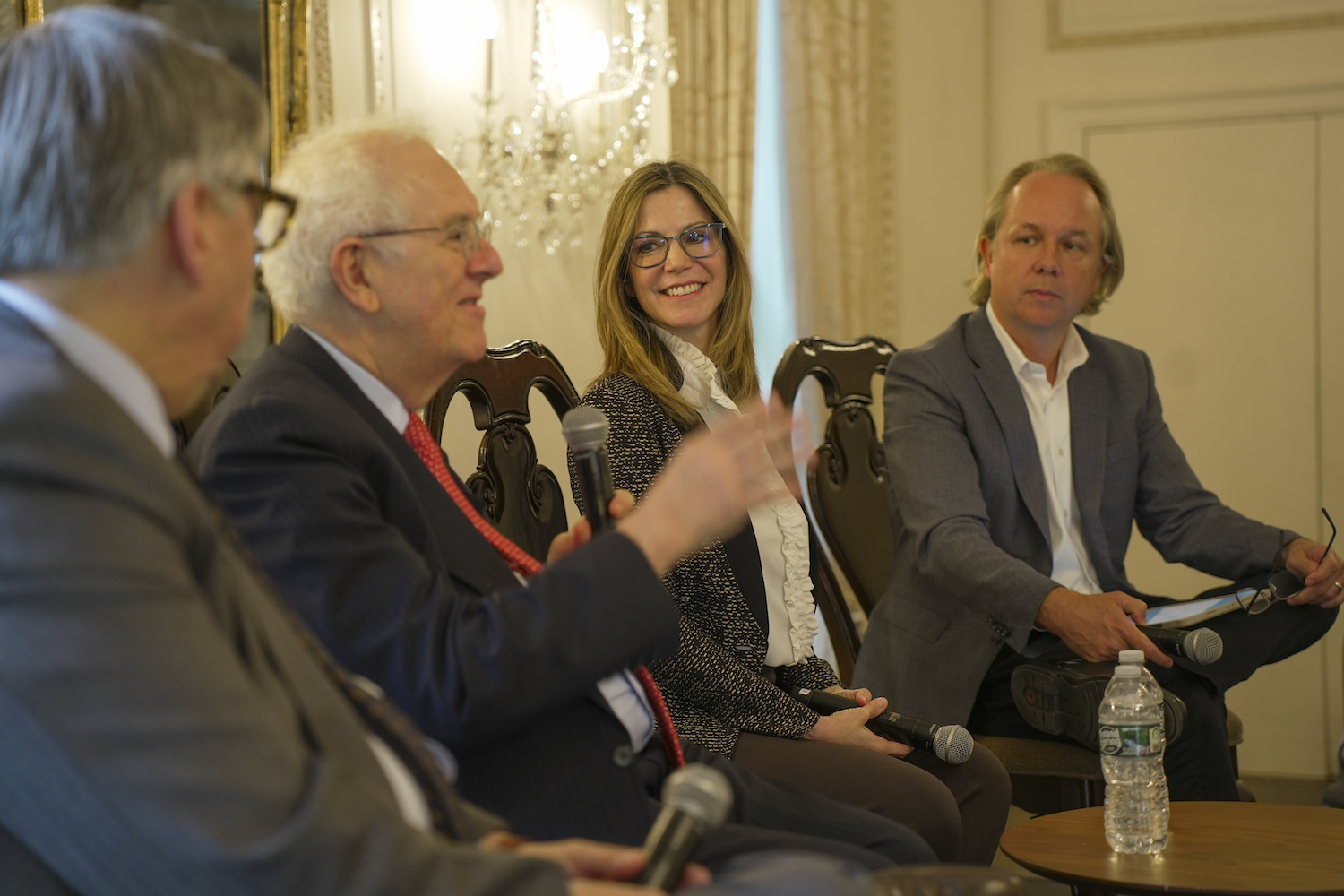 Two men and a woman listen to another man speaking into a microphone.