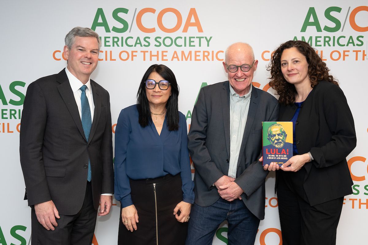 Four people stand, one holding a book, smiling in front of a backdrop.