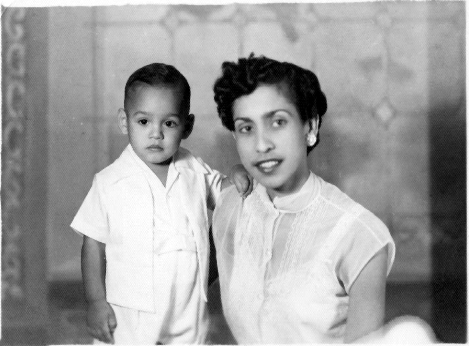 A black and white photo of a well-dressed young Latina woman with short hair posing with a young child, both in white clothing.