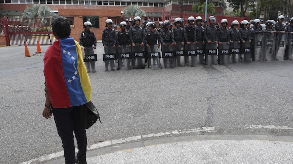 A Venezuelan citizen looks at a row of National Police in riot gear. (AP)