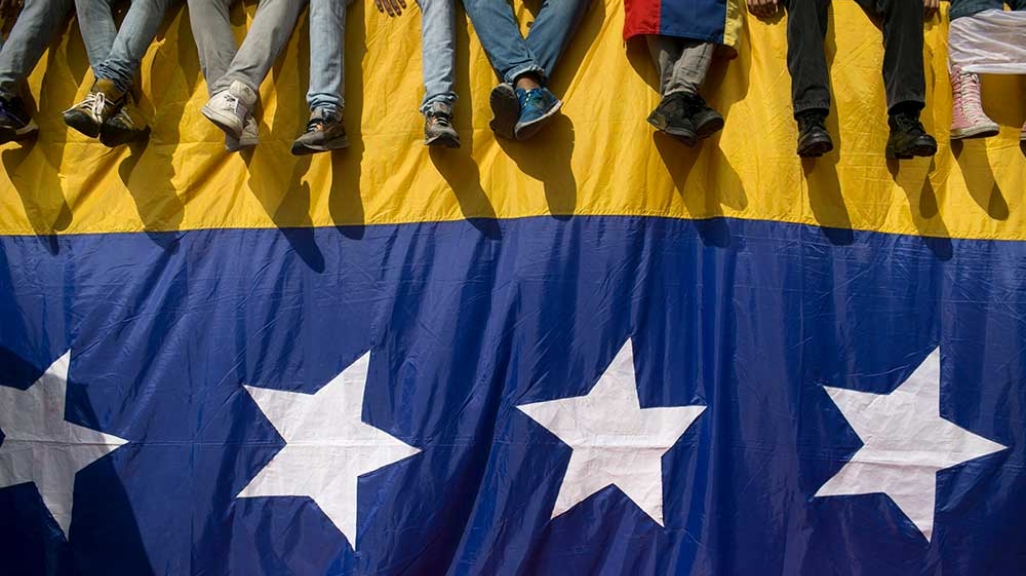 Venezuelans sit on a flag-draped wall. 