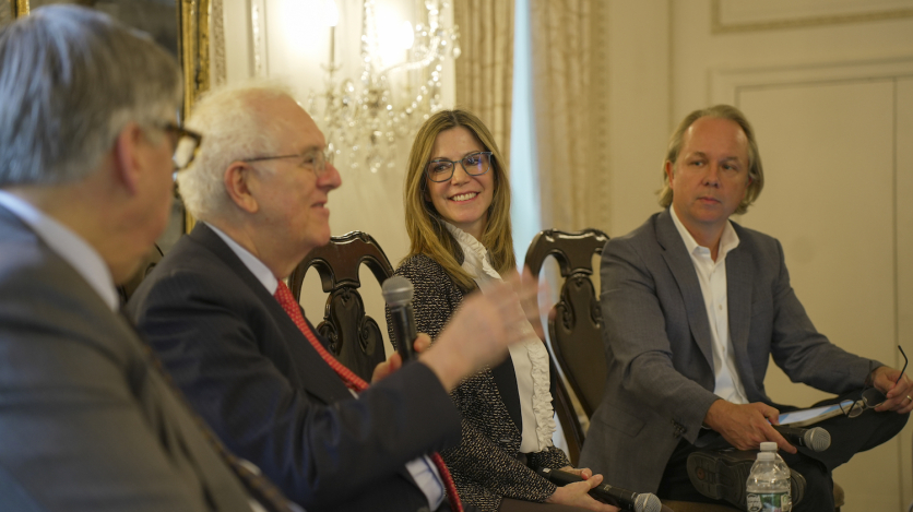 Two men and a woman listen to another man speaking into a microphone.