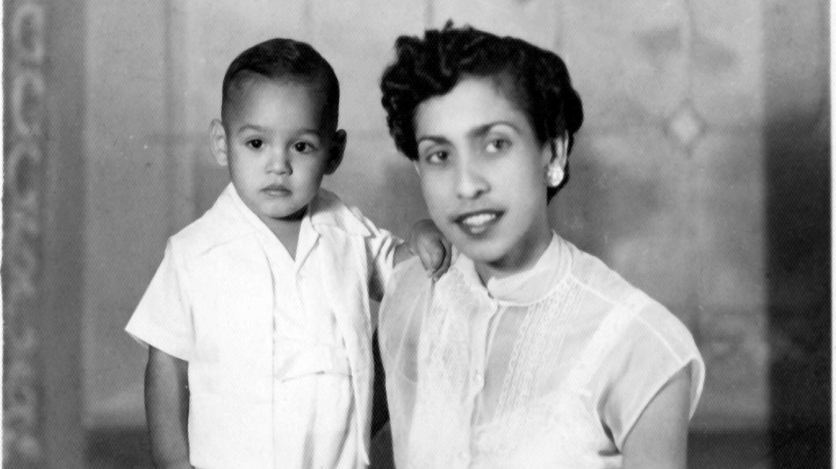 A black and white photo of a well-dressed young Latina woman with short hair posing with a young child, both in white clothing.