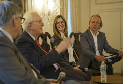 Two men and a woman listen to another man speaking into a microphone.