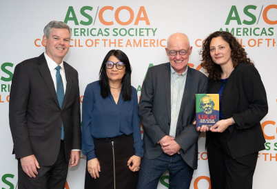 Four people stand, one holding a book, smiling in front of a backdrop.
