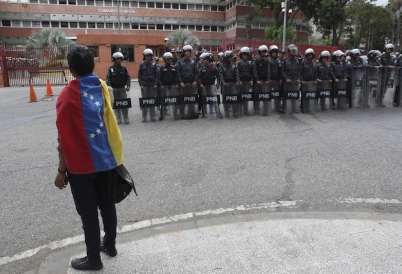 A Venezuelan citizen looks at a row of National Police in riot gear. (AP)