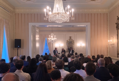 A three-person panel sits in front of a full audience in a ballroom.
