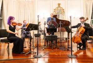 A chamber music ensemble, with accompanying accordion player, perform in a ballroom.