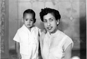 A black and white photo of a well-dressed young Latina woman with short hair posing with a young child, both in white clothing.