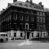 An aged photo shows a row of tall townhouses with buses going by.