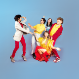 A group of five people in bright red, yellow, silver, and blue outfits pose dramatically in front of a blue background.