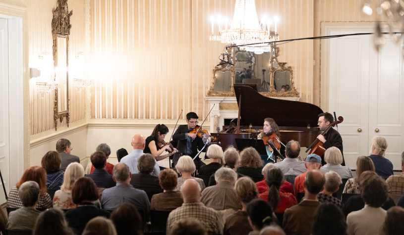 A string quartet plays in front of a small audience in a baroque ballroom.