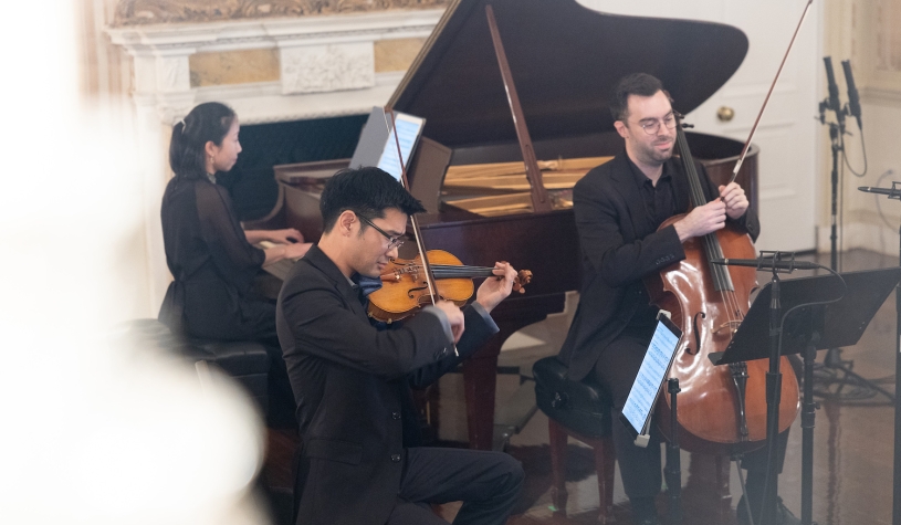 A violinist, cellist, and pianist perform.